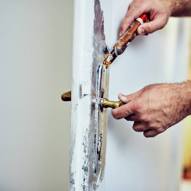 Handyman using chisel around doors lock to scrub the old paint.